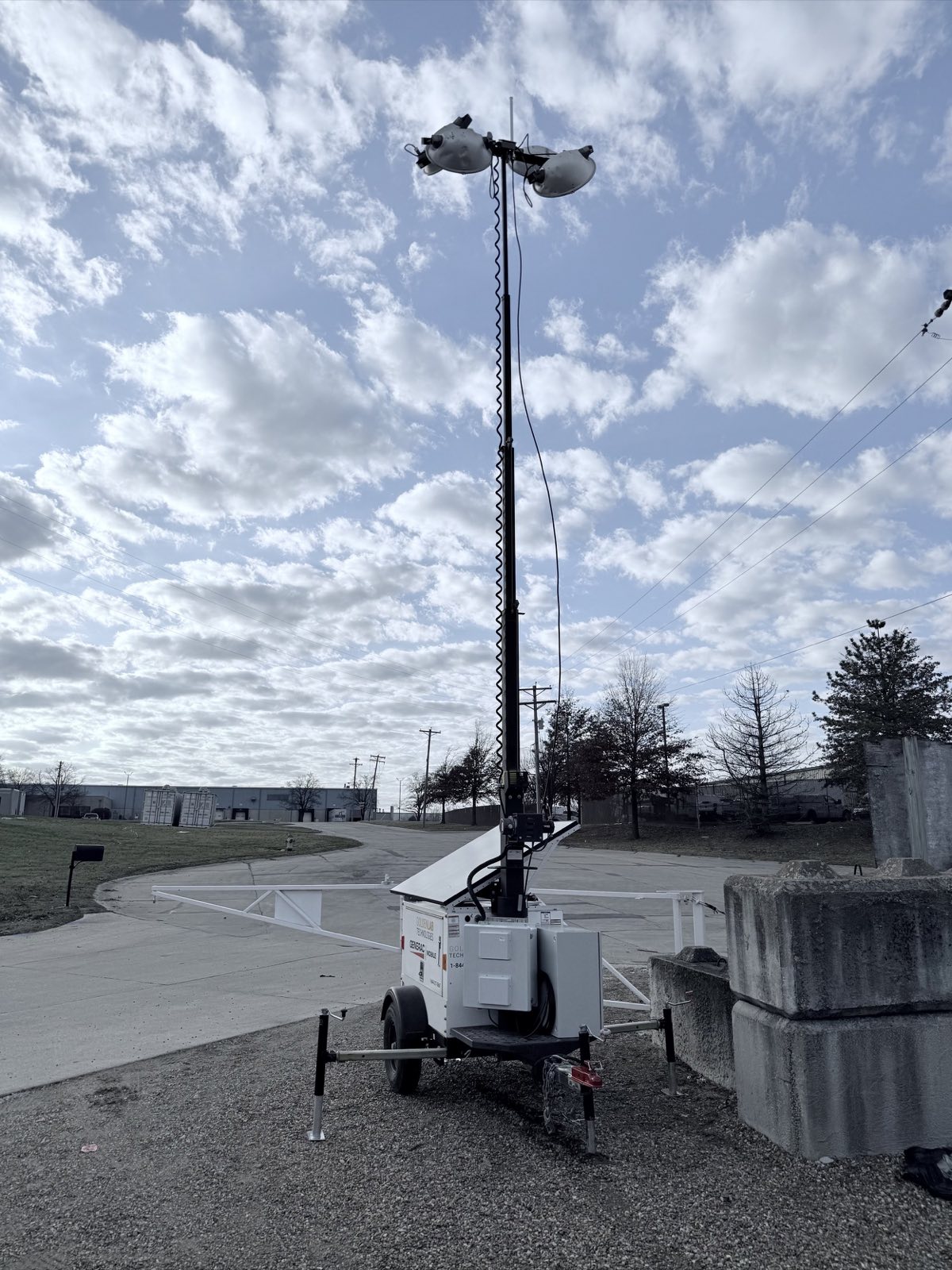 Golden Lab solar trailer with raised mast, lights and antenna parked on a gravel lot beside a concrete barrier