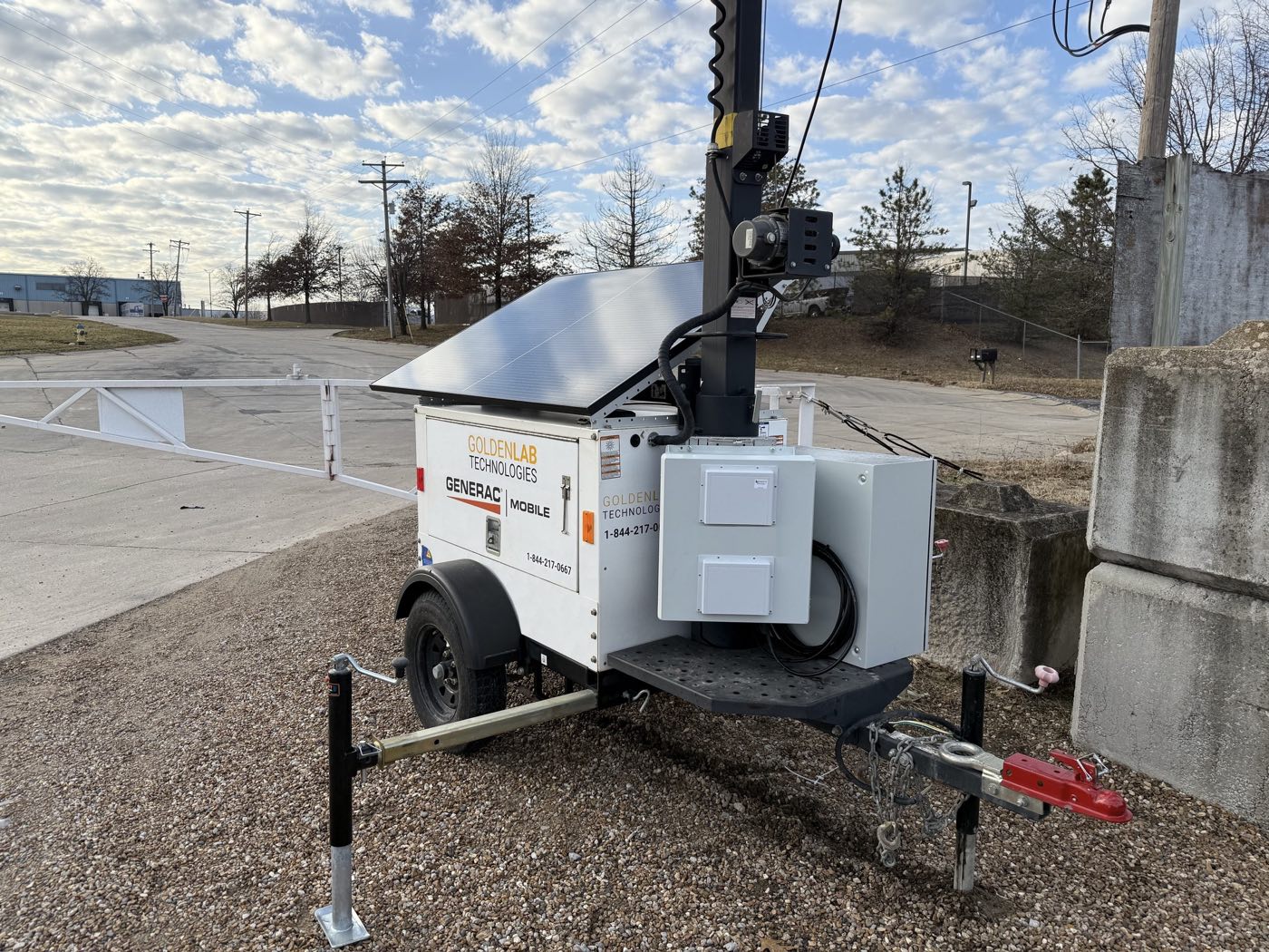 Golden Lab solar trailer with tilted solar panel, equipment cabinets and stabilizer jacks, parked on gravel